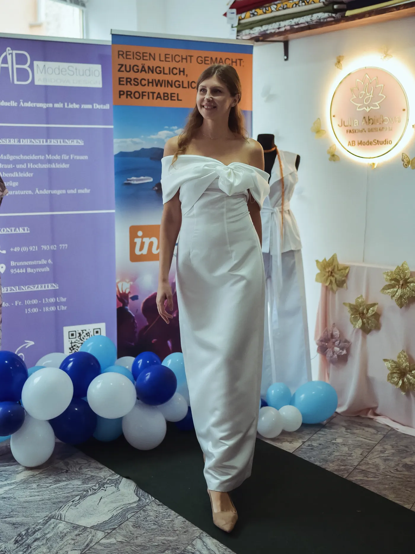 Model im weißen Kleid mit Schleife vor dem Roll-up von AB ModeStudio